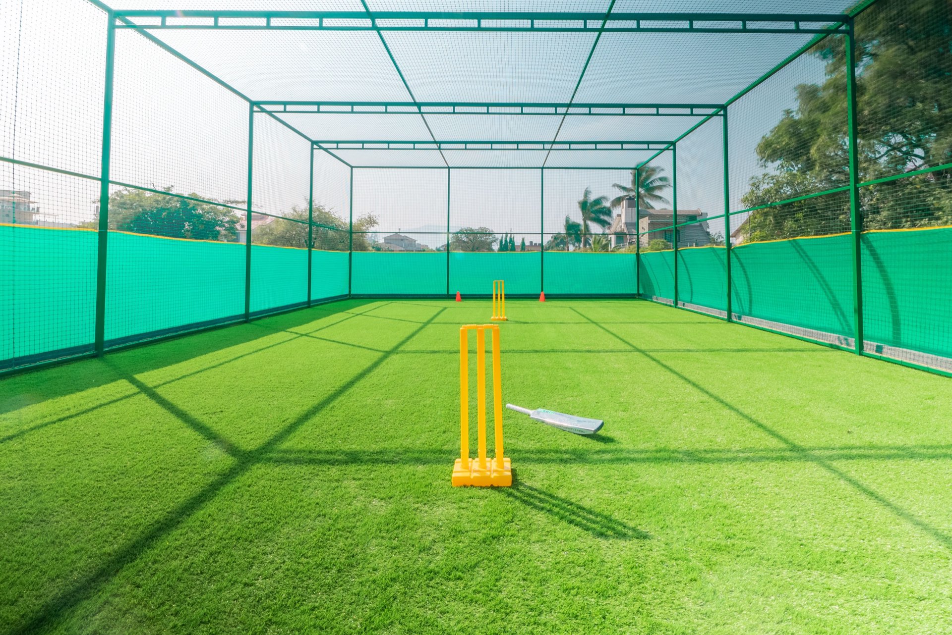 Cricket practice nets with stumps and a bat on the turf