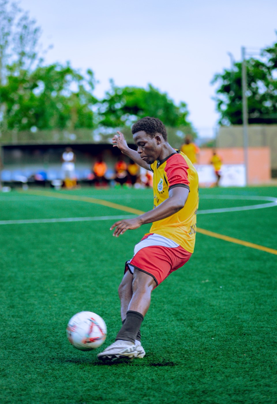 A footballer in a yellow shirt striking the ball on an artificial pitch