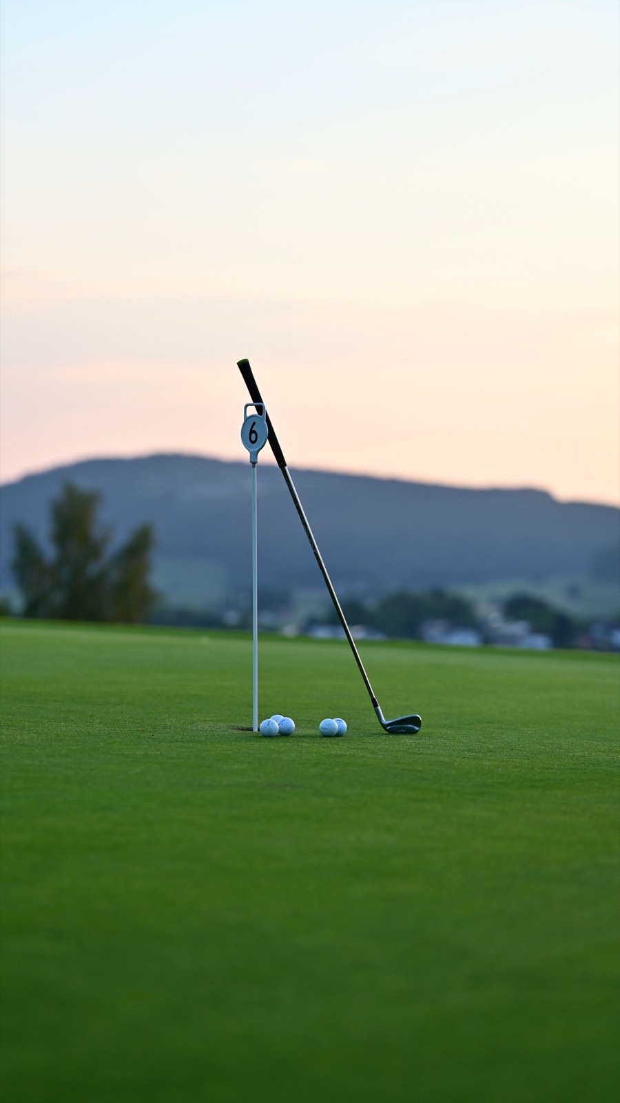 An empty green at dusk, a club and balls left by the flag